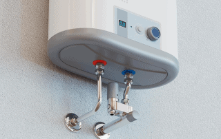 A close-up of the underside of a wall-mounted water heater showing control buttons, a power knob, and two connected pipes with red and blue markings for hot and cold water.